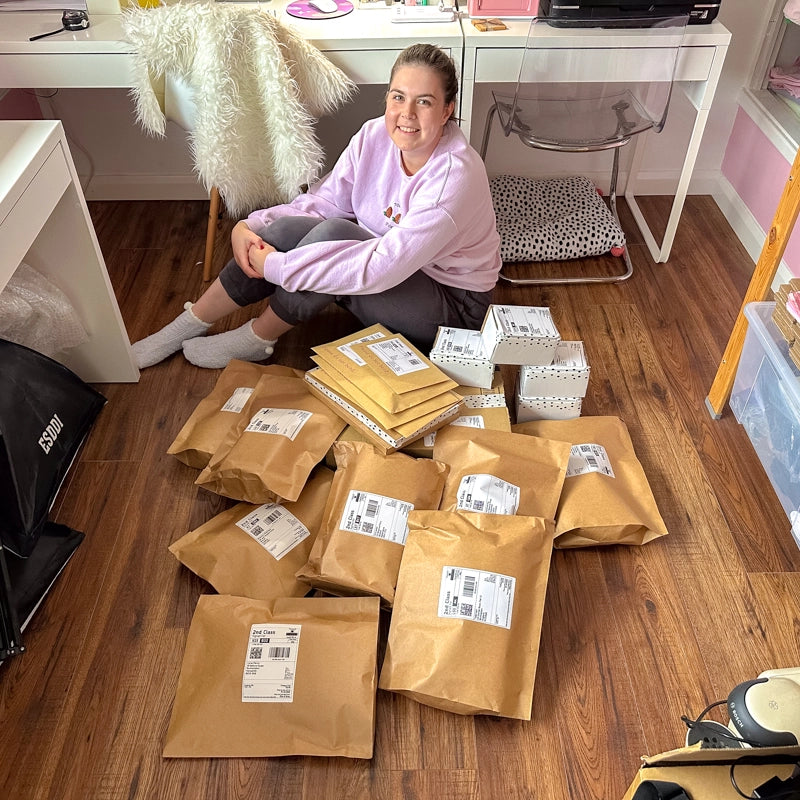 Holly, the owner of Sprinkle Club, sitting happily among a pile of neatly packaged orders ready for dispatch in her cosy, pink-themed office