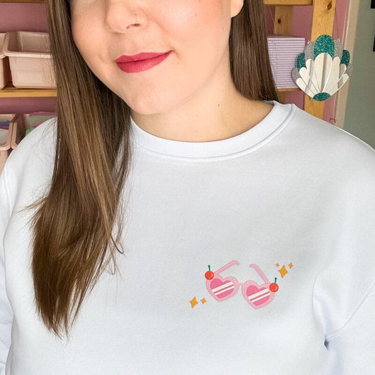 Sprinkle Club - A woman swearing a white valentine's sweatshirt with a love heart sunglasses illustration on the left breast