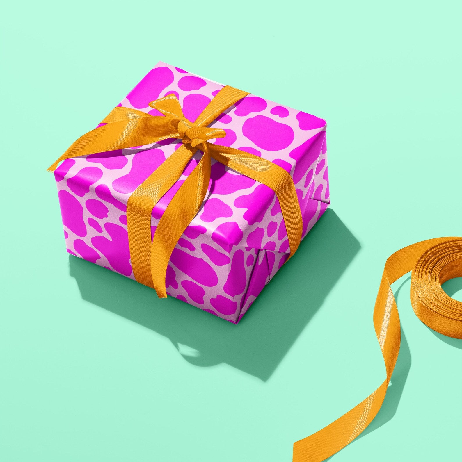 Sprinkle Club - A present wrapped in pink cow print wrapping paper and tied in an orange ribbon bow