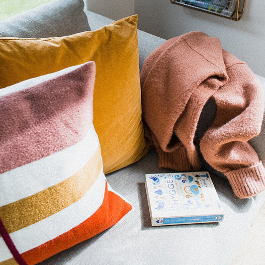 Sprinkle Club - A sofa at home with two colourful cushions a cardigan and a book