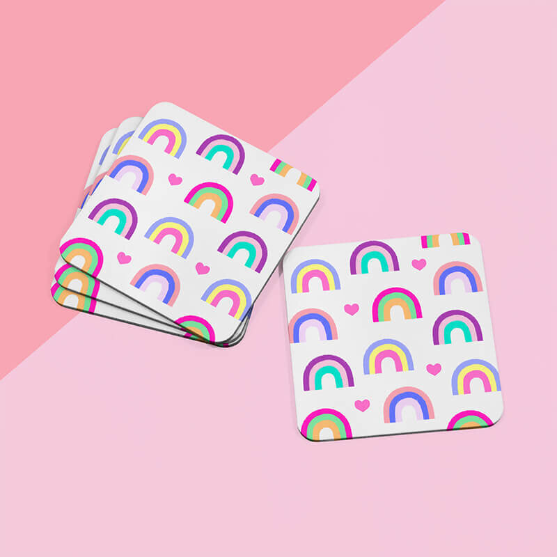 Sprinkle Club - Multiple colourful rainbow and heart square drinks coasters fanned out on a dual-tone pink surface