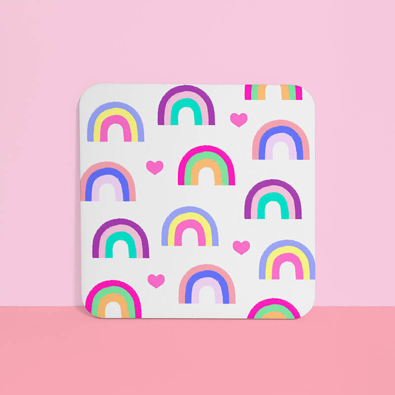 Sprinkle Club - White square drinks coaster with colourful rainbow patterns and hearts, centered on a soft pink background