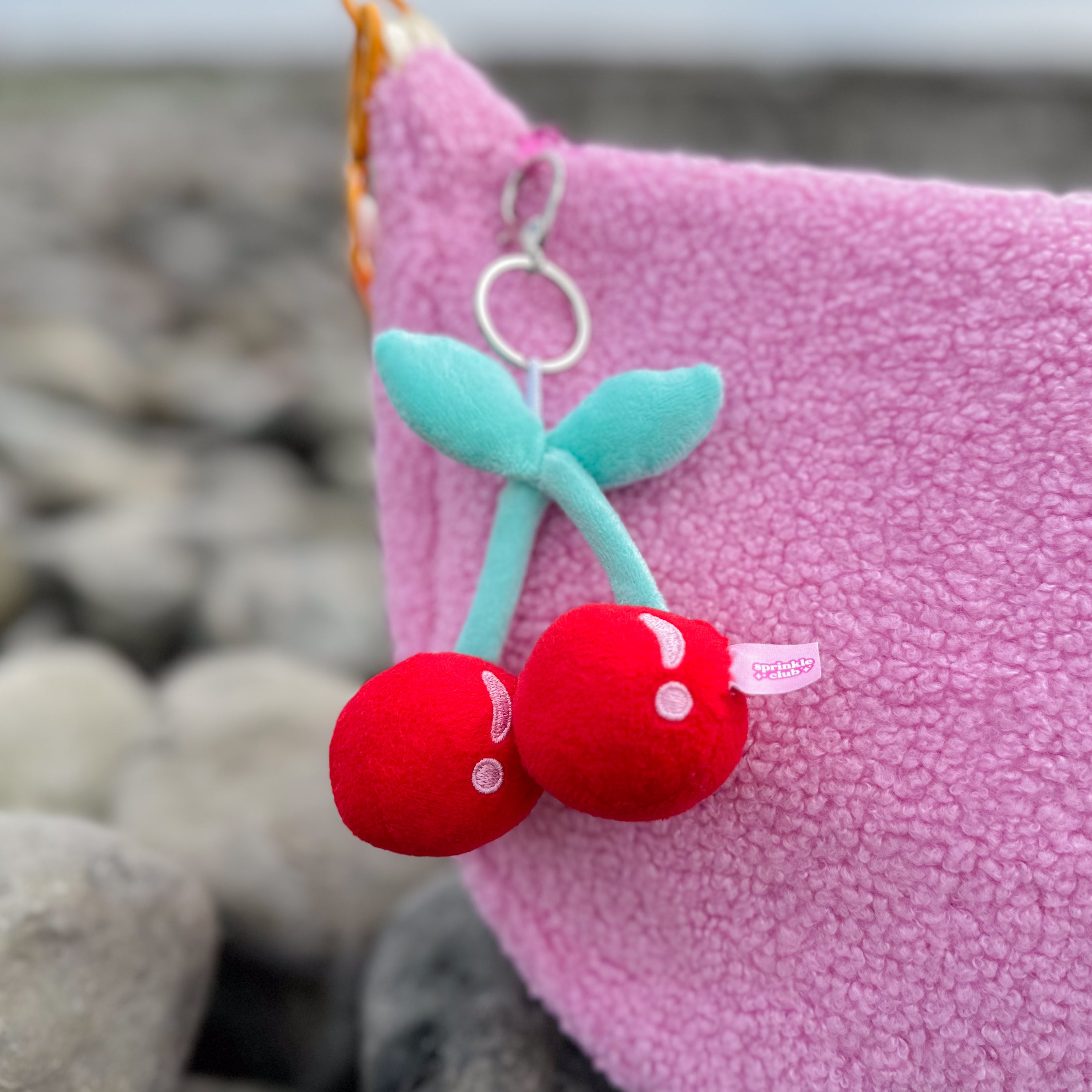 Cherry plushie keychain clipped to pink teddy bag – cute red fruit charm with pastel green stems, kawaii bag accessory by Sprinkle Club