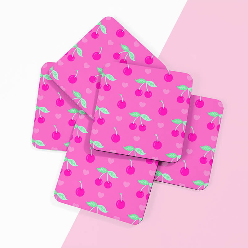 Sprinkle Club - Multiple pink square drinks coasters with cherry and heart motifs spread out on a pink surface