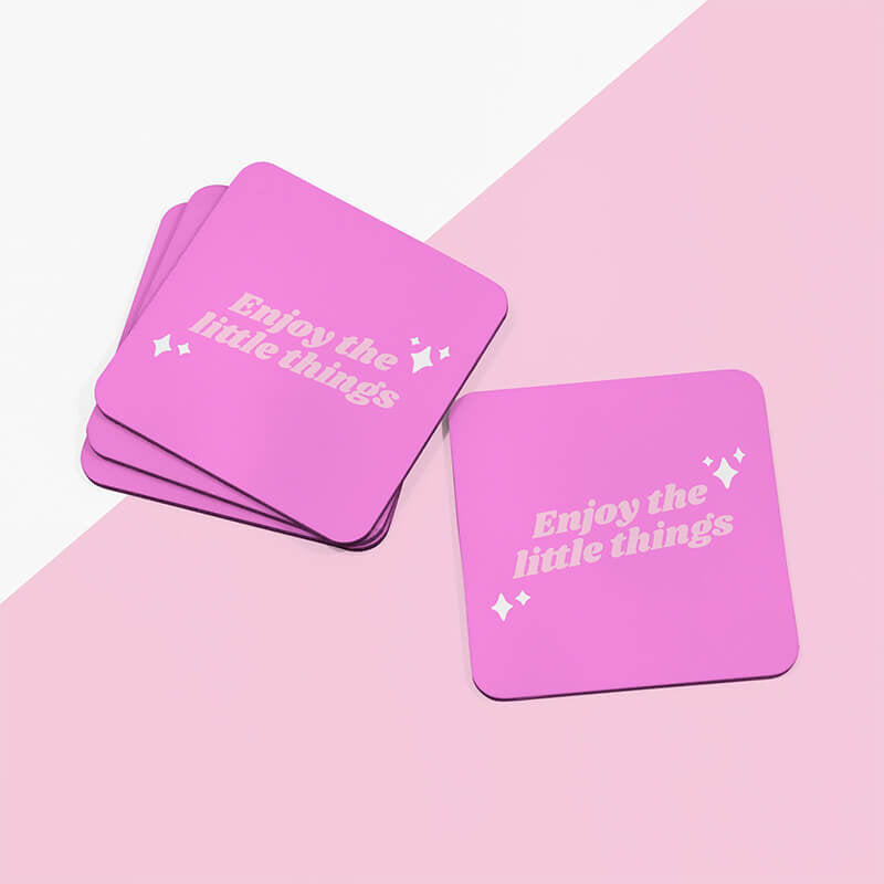 Sprinkle Club - A stack of vibrant pink square coasters with 'Enjoy the little things' in playful light pink lettering, arranged haphazardly on a dual-tone pink surface
