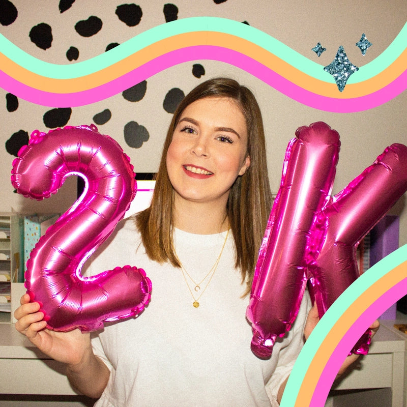 Holly, founder of Sprinkle Club, cheerfully holding magenta '21K' balloons to celebrate a follower milestone, with a whimsical background of pastel wavy lines and sparkly accents
