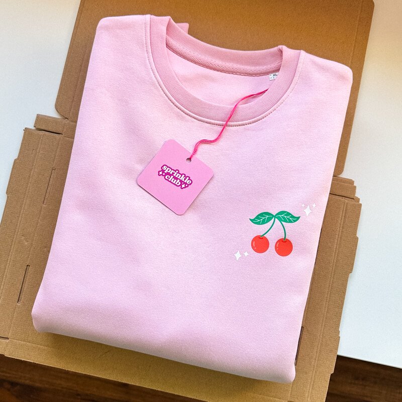 Sprinkle Club - A folded pink and red valentine's sweatshirt with a cute cherry illustration design