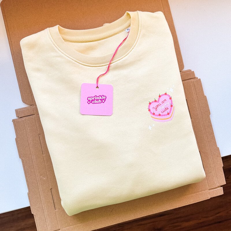 Sprinkle Club - A folded pastel yellow sweatshirt with a vintage cake illustration