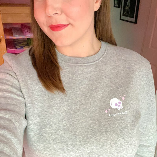 Sprinkle Club - Woman wearing a grey halloween sweatshirt with a cute skull illustration and the text 'cute as hell' on the left breast