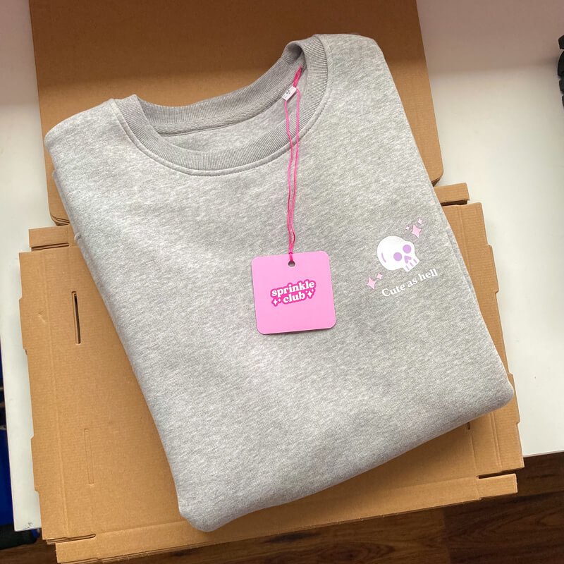 Sprinkle Club - A women's folded grey halloween sweatshirt with a cute skull illustration and a pink swing tag