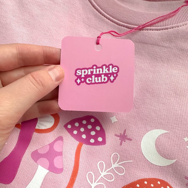 Sprinkle Club - A pink swing tag attached to a pink witch inspired sweatshirt design