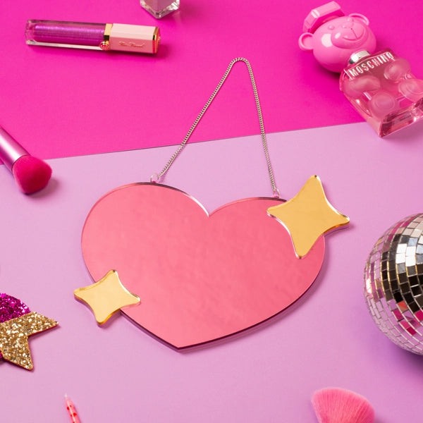 Sprinkle Club - A small pink heart shaped mirror with gold mirrored sparkles in the top right and bottom left with a chain to hang on the wall
