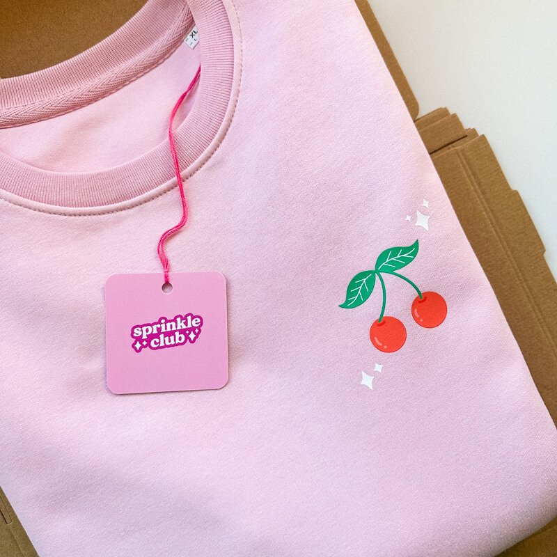 Sprinkle Club - Folded pink sweatshirt with a cherry illustration design