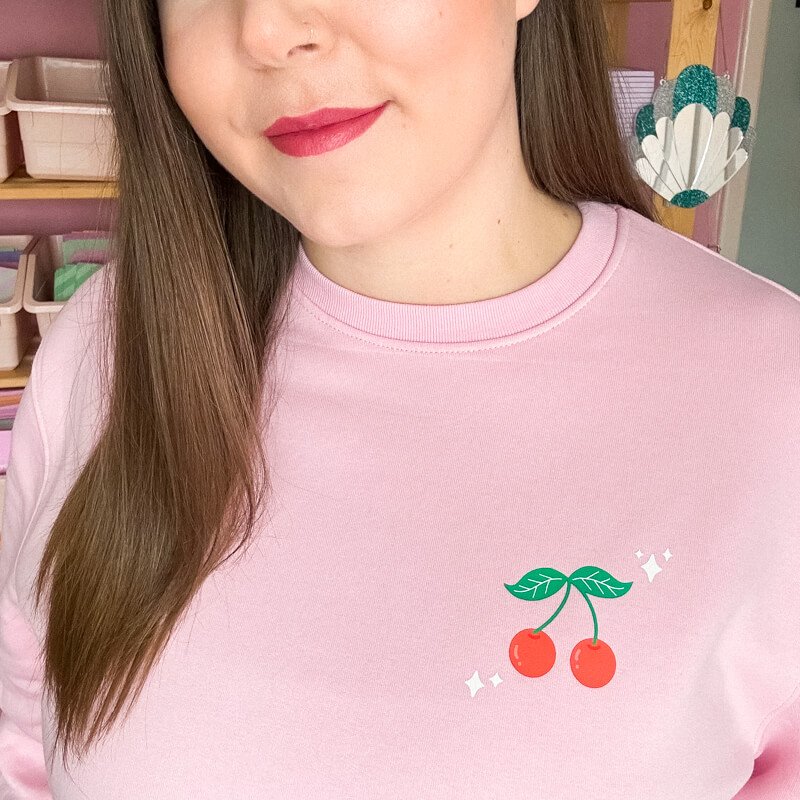 Sprinkle Club - A woman wearing a pink valentine's sweatshirt with a red cherry illustration on the left breast