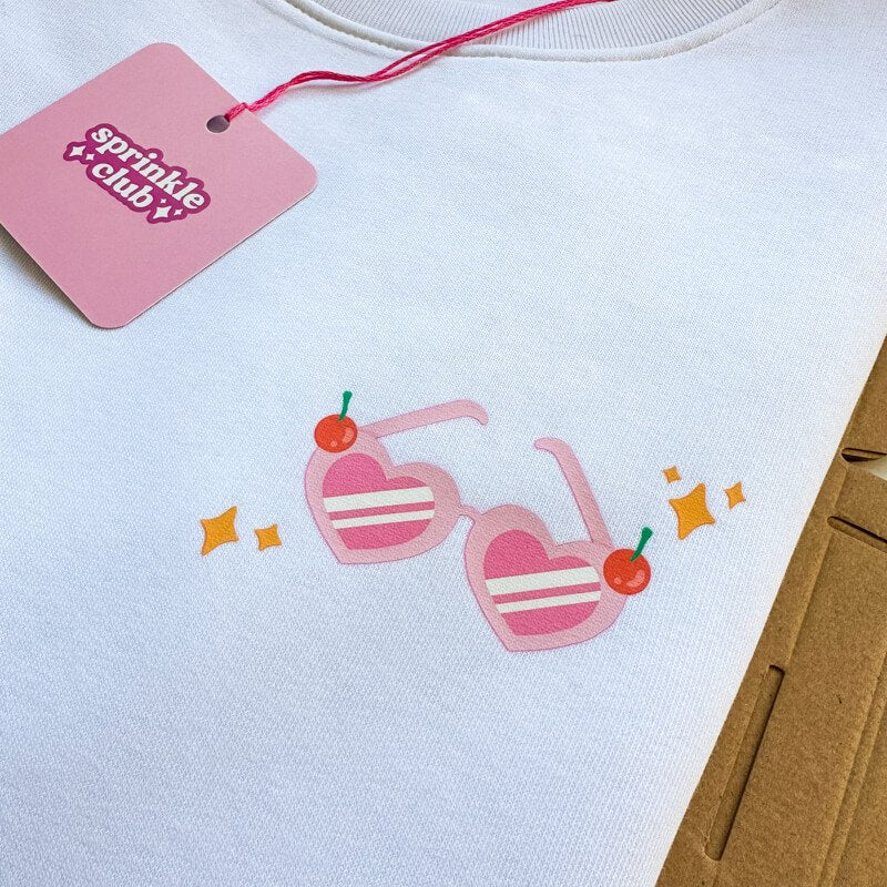 Sprinkle Club - A close up of a love heart sunglasses illustration on a white organic sweatshirt