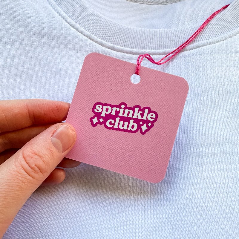Sprinkle Club - A pink swing tag attached to a white valentine's sweatshirt