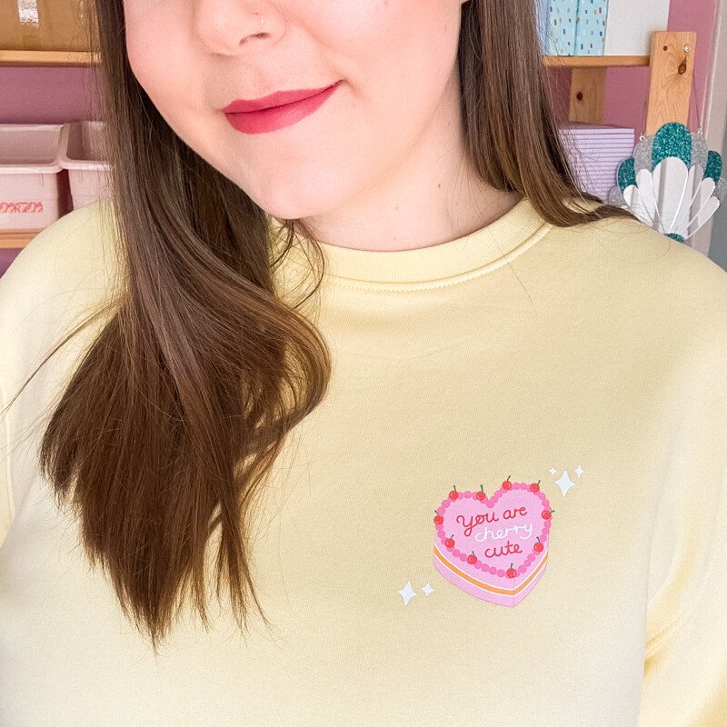 Sprinkle Club - Woman wearing a pastel yellow sweatshirt with a pink vintage cake illustration on the left breast