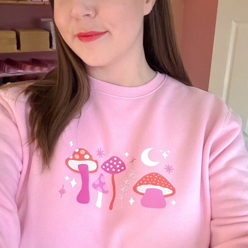 Sprinkle Club - A woman wearing a pink and red mushroom witch inspired sweatshirt with stars and a crescent moon
