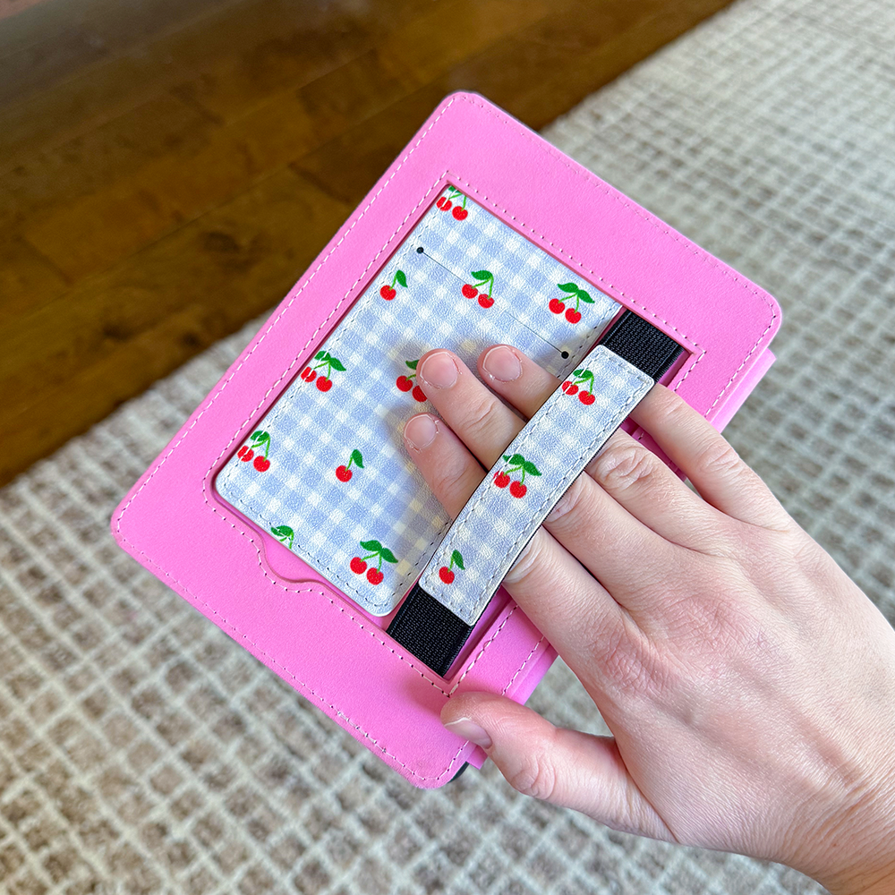 Sprinkle Club - Pink kindle case with a blue gingham pattern featuring red cherries held by a hand on a textured surface