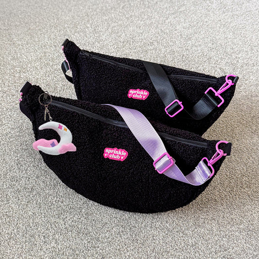 Two black fluffy teddy crossbody bags with pink Sprinkle Club logo patches and pink hardware, one with a lilac strap and moon plushie keychain, one with a black strap