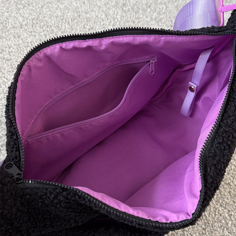 Inside of the black fluffy teddy crossbody bag, unzipped to show the purple lining, an internal zip pocket and a lilac snap-fastening key strap