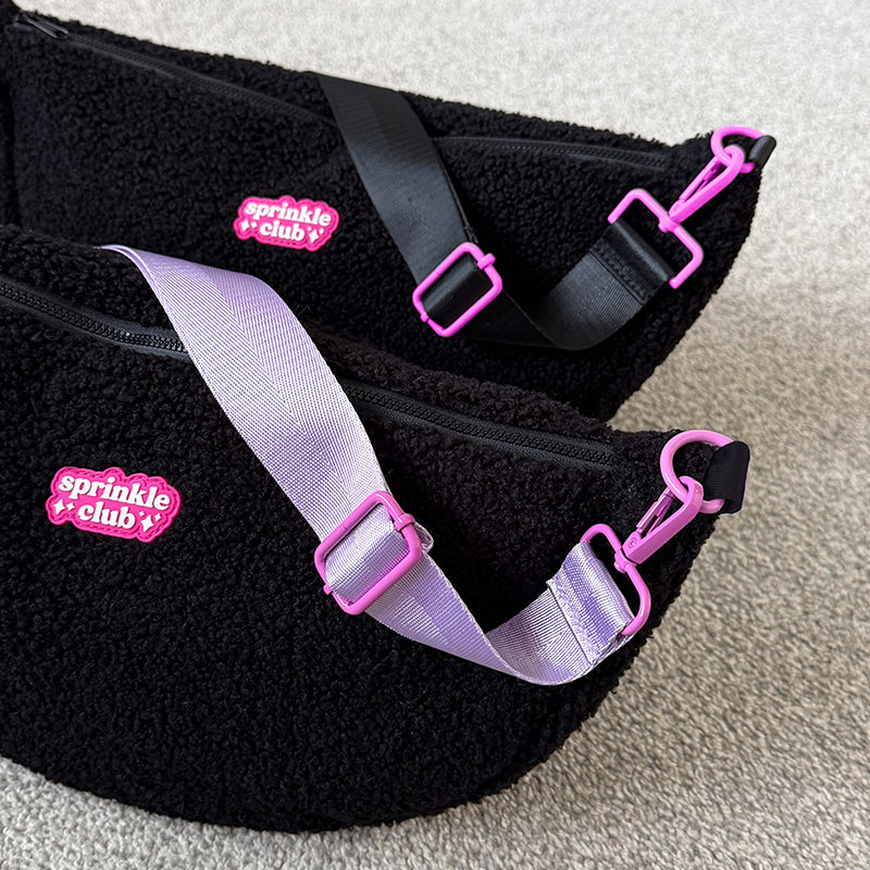 Close-up of two black fluffy teddy crossbody bags showing pink strap clips and sliders on a lilac strap and a black strap, with pink Sprinkle Club logo patches
