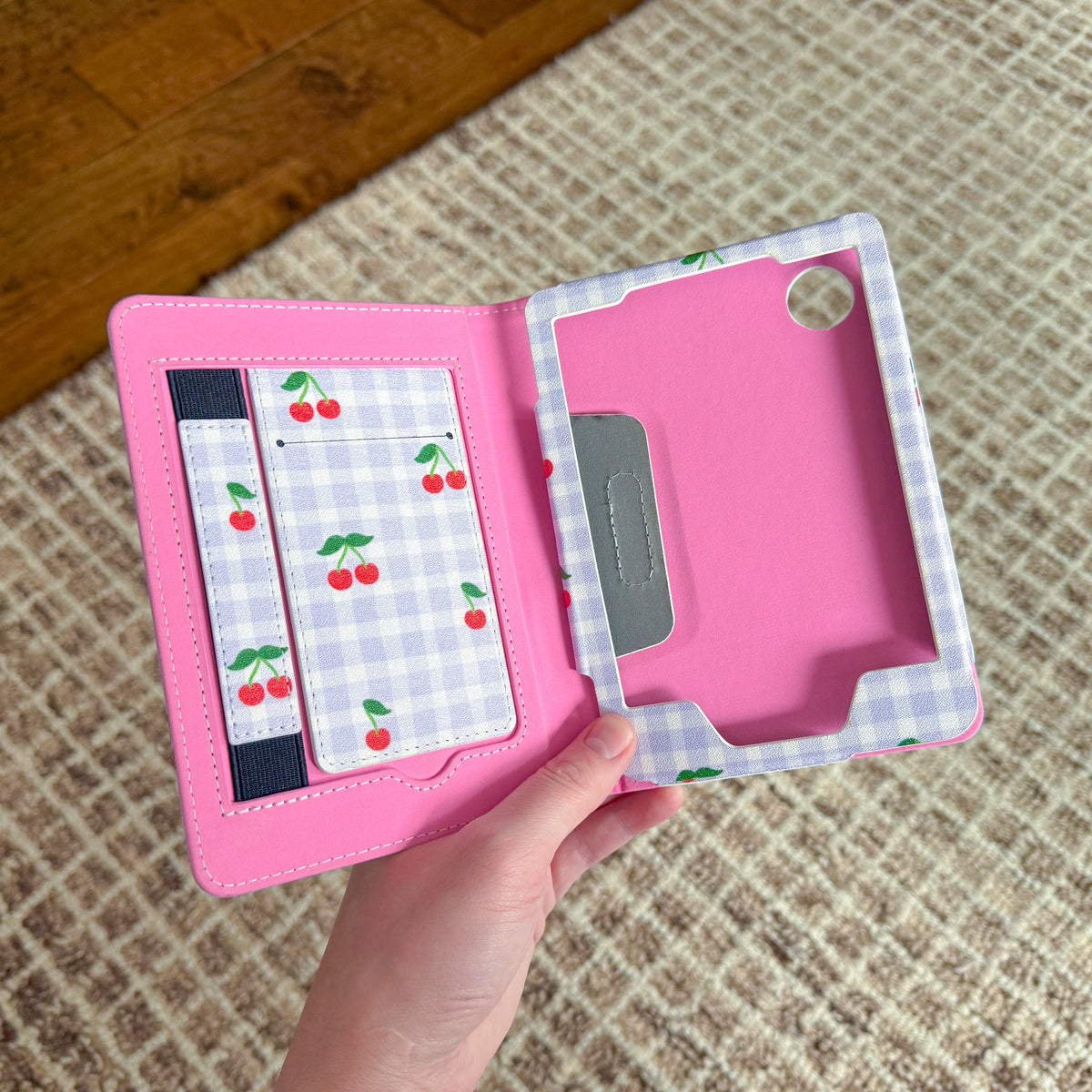 Cherry gingham Kobo Clara case held open, showing a bright pink interior with a cherry gingham fold-out stand and hand strap inside the cover