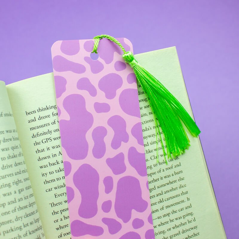 Sprinkle Club - A lilac bookmark with a cow print pattern and a bright green tassel against a purple background