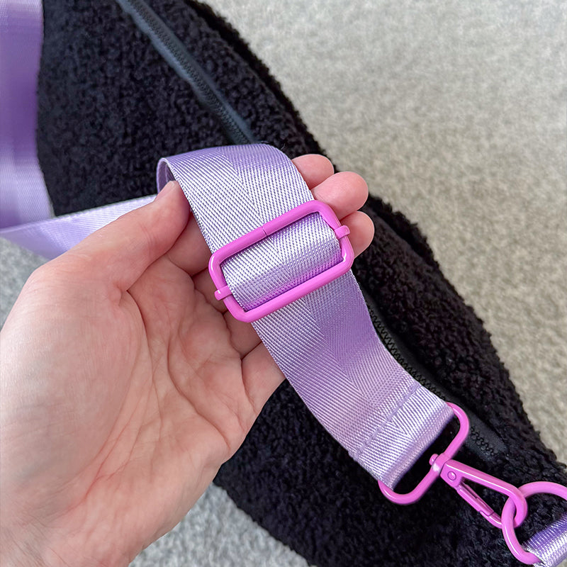 Hand holding the lilac adjustable strap of a black fluffy teddy crossbody bag, showing the pink slider buckle and clip