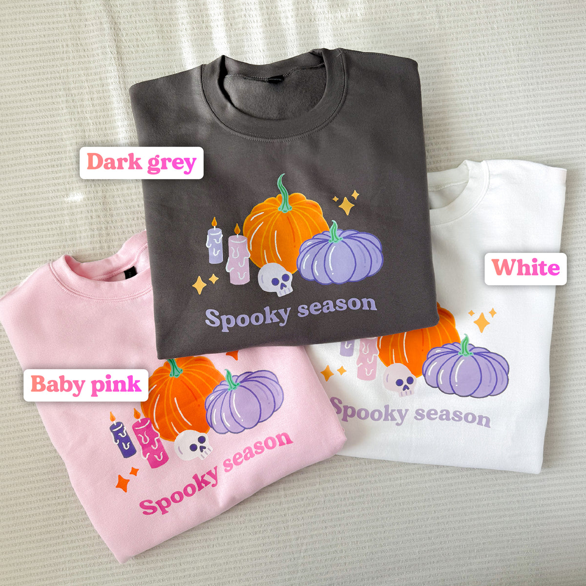 Pastel Halloween pumpkin sweatshirt in three colours laid flat, labelled dark grey, baby pink and white