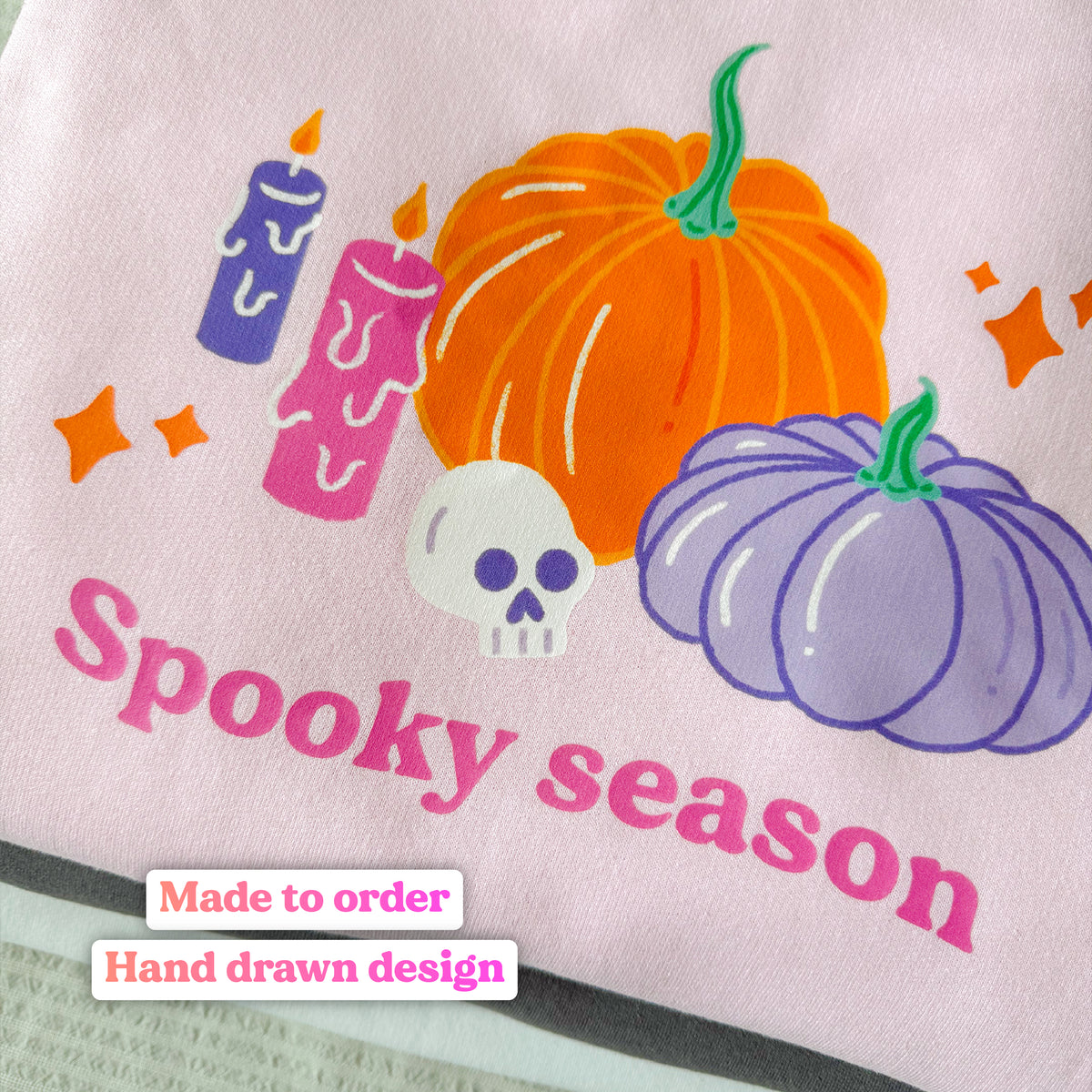 Close-up of the hand drawn Spooky season pumpkin print on the baby pink sweatshirt, labelled: made to order, hand drawn design