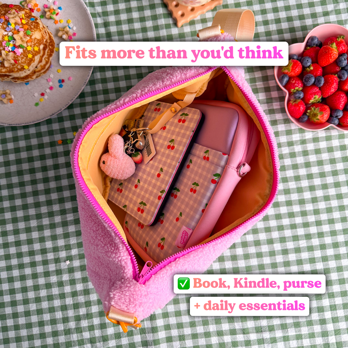 Open pink fluffy teddy crossbody bag from above, holding a cherry gingham e-reader case, a padded pink case and keys, with text reading "Fits more than you'd think: book, Kindle, purse and daily essentials"