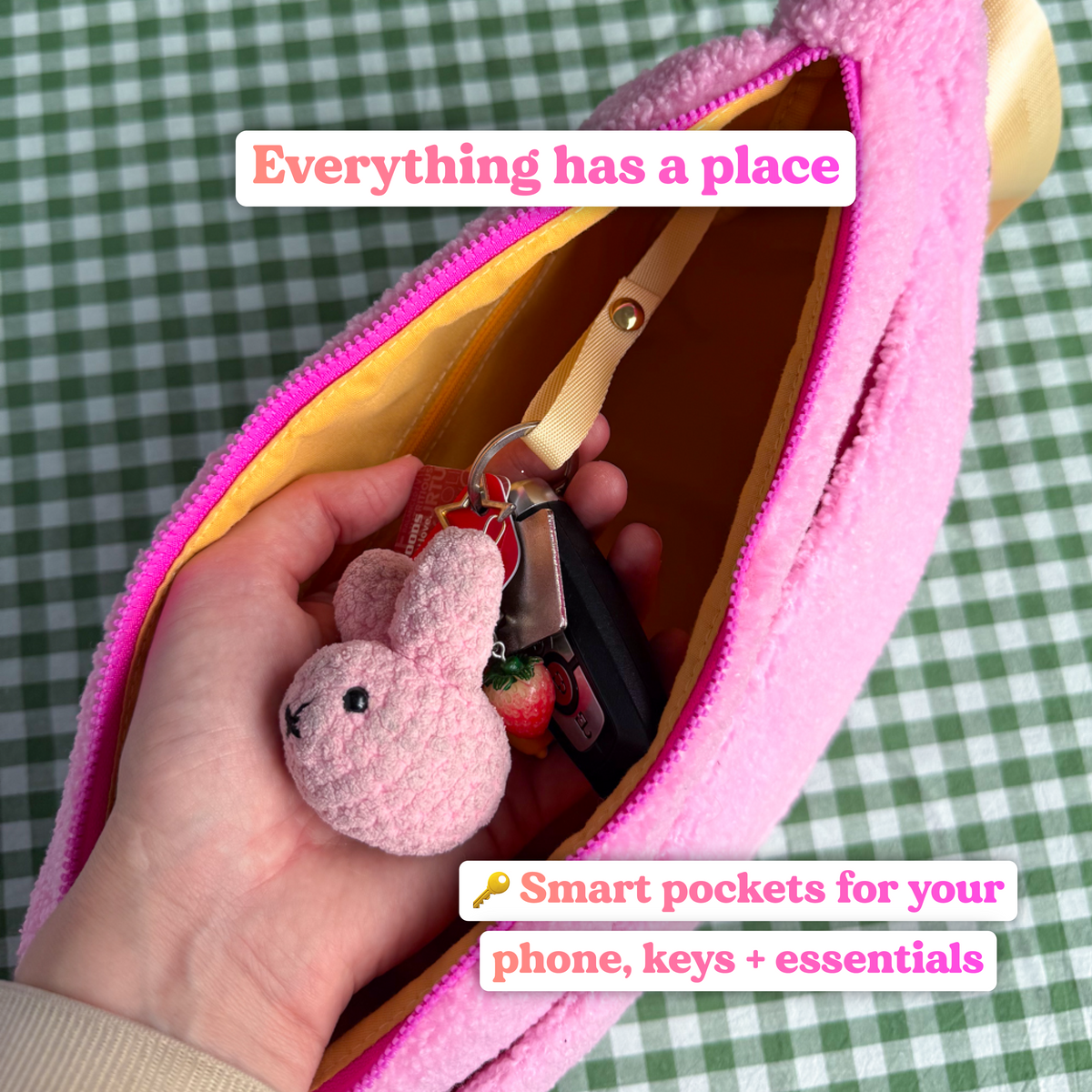 Hand holding a set of keys with a pink bunny keyring, clipped to a key strap inside the open pink fluffy crossbody bag, with text reading "Everything has a place: smart pockets for your phone, keys and essentials"