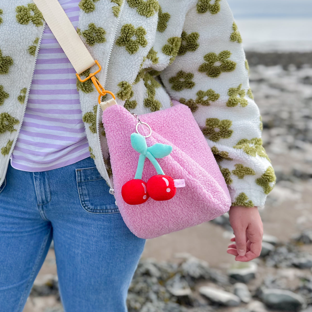 Pink teddy crossbody bag worn at the hip with adjustable strap and cherry plushie keychain