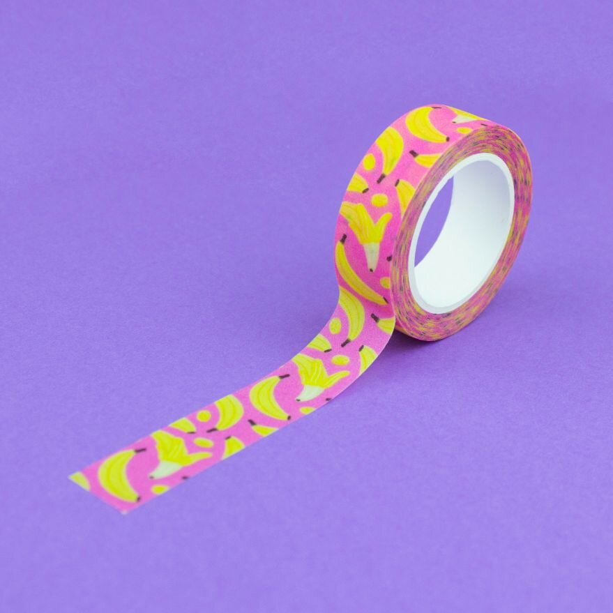 A single roll of pink and yellow banana fruit washi tape unraveled on a purple background
