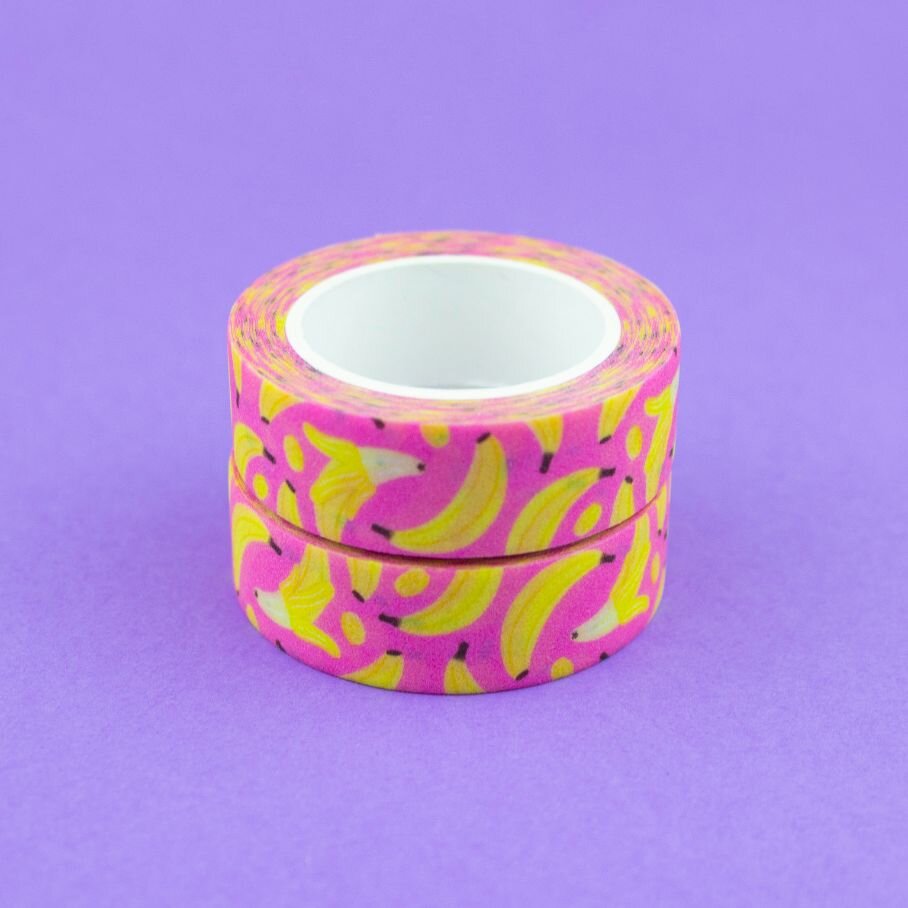 Two stacked rolls of pink and yellow banana fruit washi tape on a purple background