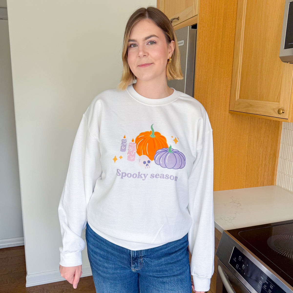 Woman wearing the white pastel Halloween pumpkin sweatshirt loose over blue jeans, showing the relaxed crewneck fit